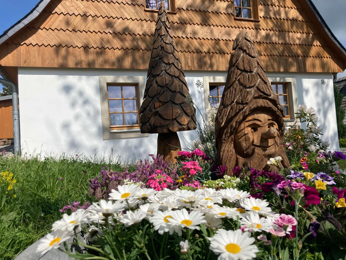 Gartenbereich mit Holzskulptur und Blumen vor traditionellem Haus